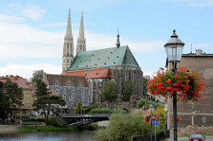 Blick vom Zgorzelec - Ufer der Lausitzer Neiße; Laternenmast mit blühenden Geranien - im Hintergrund die evangelische Pfarrkirche St. Peter und Paul und das Waidhaus.