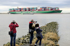 Fotografen am Elbufer bei Grünendeich auf einer Steinbuhne - auf der Elbe, der auf einer Sandbank festgefahrene Containerfrachter CSCL Indian Ocean.