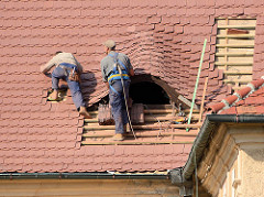 Dachdecker bei der Arbeit - ein Dachfenster / Ochsenauge wird mit Ziegeln eingedeckt; Gebäude des Franziskaner Klosters in Kłodzko / Glatz.