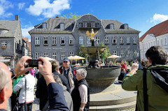 Touristen auf dem Marktplatz von Goslar - Blick zum Kaiserringhaus, ehem. Kämmereigebäude - an dessen Giebel ist eine Uhr. Viermal am Tag öffnen sich die drei darunter befindlichen Türen und eine Figurengruppe in Bergmannstracht erscheint. Diese b