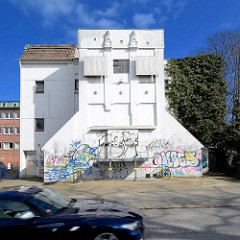 Historische Industriearchitektur im Hamburger Stadtteil Eimsbüttel  - Lagergebäude mit weisser Fassade und Grafitti, Figuren unter dem Flachdach.