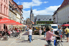 Wochenmarkt am Marktplatz von Quedlinburg - Verkaufsstände mit Obst und Gemüse; Cafés und Restaurant mit Tischen auf der Strasse - Gäste sitzen unter Sonnenschirmen in der Sonne; im Hintergrund das Rathaus und die Marktkirche / St. Benedikt Kirch
