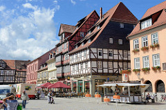 Historische Bebauung - mehrstöckige Fachwerkhäuser am Marktplatz von Quedlinburg; Imbisswagen und Aussengastronomie mit Sonnenschirmen auf der Straße.