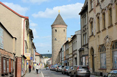 Straßenansicht der Straße Havlíčkova in Dvůr Králové nad Labem / Königinhof an der Elbe; Passanten auf dem Gehweg - parkende Autos;  im Hintergrund ein alter Wehrturm der ehem. Stadtbefestigung.