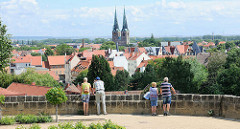 Touristen blicken vom Schlossberg auf die Dächer der Welterbestadt Quedlinburg - Hausdächer und Kirchtürm der St. Nikolaikirche.