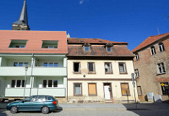 Neu + Alt - Wohnhäuser in Aschersleben; Neubau mit Balkons und ausgebautem Dach, mintgrün gestrichene Hausfassade; daneben eine leerstehende Hausruine mit vernagelten Fenstern.