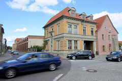 Strassenverkehr in Aschersleben - Strassenkreuzung; Grunderzeitgebäude mit gelben Ziegeln, Fassadenaufschrift Samen Handlung; im Hintergrund die WEMA Halle.