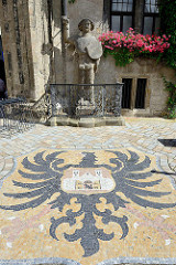 Wappen von Quedlinburg als Mosaik im Boden vor dem Rathaus eingelassen, dahinter der Quedlinburger Roland, der neben dem Roland von Bremen und Halberstadt eine der ältesten Rolandfiguren ist.