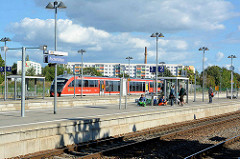 Bahnhof von Aschersleben - Regionalzug und wartende Fahrgäste, im Hintergrund ein Hochhaus / Wohnblock mit farbigen Balkons.