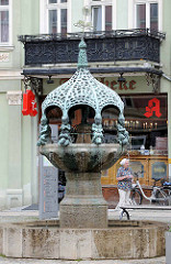 Hennebrunnen in Aschersleben; die Brunnenanlage zeigt eine durch einen Baldachin überdachte gegliederte Säule, auf der acht eigenartige Bronzeputten sitzen. Der Brunnen wurde von Georg Wrba entworfen und 1906 eingeweiht.