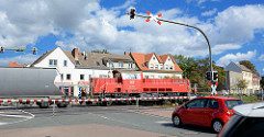 Bahnübergang in Aschersleben; die Schranken sind herunter gelassen, ein Güterzug mit Lokomotive / Lok 251 019-4 der Deutschen Bahn kreuzt die Strasse - wartende Autos.