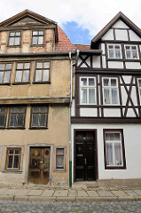 Alt + Neu, Fachwerkhäuser in Quelinburg - re. restauriert mit gestrichener Fassade - lks. grauer Rauputz und abblätternde Farbe / leerstehendes Gebäude.