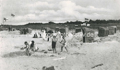 Historische Aufnahme vom Badeort, Ostseebad Zingst - Sandburgen mit Strandkörben, Kinder spielen in Kleidung, Matrosenanzug im Sand; Flaggen Deutsches Reich und Flagge Deutsche Kaiserliche Marine wehen am Strand.