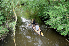 Wasserlauf Rathauswettern zwischen Erlen - Wasserweg in Hamburg Wilhelmsburg / Inselpark; ein Kanu fährt auf dem Kanal.