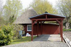 Kleines reetgedecktes Holzhaus, Ferienhaus mit großem Carport, dahinter Einfahrt zur Garage.