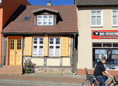 Denkmalgeschütztes Wohnhaus in der Fischerstraße von Ribnitz-Damgarten - gelb / weiß abgesetzte Tür und Fensterluken, daneben ein schlichter Putzbau.