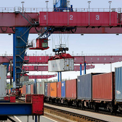 Die Ladung eines Containerzugs wird im Containerbahnhof Hamburg Altenwerder gelöscht - einer der Container wird mit einem Portalkran vom Güterwaggon zum Sattelauflieger transportiert.