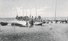 Historisches Bild vom  Ostseebad Zingst - eine Holzbrücke, Seebrücke führt ins Wasser - Menschen stehen auf dem Steg; am Strand liegen Ruderboote, Fischerboote.