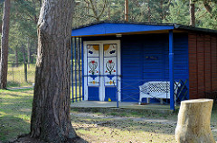Kleines Ferienhaus zwischen Kiefern;  Holzhaus mit kleiner Veranda und Plastikbank - bunte mit Eisenriegel gesicherte Eingangstür / Ostseebad Prerow.