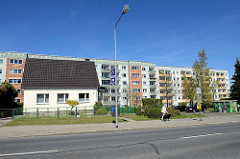 Einzelhaus mit Satteldach und weißer Hausfassade an der Rostocker Straße in Ribnitz-Damgarten - im Hintergrund mehrstöckige Wohnblocks / Hochhäuser; Fussgängerin mit Hund.
