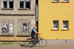 Restauriertes Wohnhaus mit gelb gestrichener Fassade, verfallenes Gebäude mit abbröckelndem Putz und Luken verschlossene Fenster - Fahrradfahrer; Architekturbilder aus Barth  / Alt + Neu.