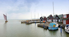 Ferienhäuser am Wasser, Hafen von Altenhagen / Ostseebad Ahrenshoop. Ein Zeesenboot fährt in den Saaler Bodden. Das Zeesenboot ist ein Fischerboot und hat einen geringen Tiefgang - so ist es sehr gut geeignet für das Fischen in den flachen Küsten- un