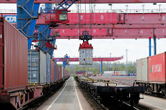 Die Ladung eines Containerzugs wird im Containerbahnhof Hamburg Altenwerder gelöscht - einer der Container wird mit einem Portalkran vom Güterwaggon zum Sattelauflieger transportiert.