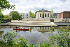 Blick über die Rathauswettern zur Industriearchitektur vom ehem. Wasserwerk in Hamburg Wilhelmsburg - Fahrräder auf der Promenade, ein Kanu fährt auf dem Entwässerungsgraben.