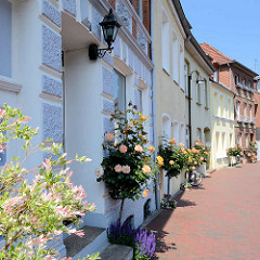 Straße in Mölln - Hauseingänge mit blühende Rosen / Stockrosen bepflanzt.