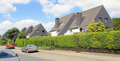 Einstöckige Doppelhäuser mit vier Wohneinheiten und gemeinsamen Schornsteine - unterschiedliche Heckengestaltung.