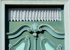 Detail einer Schmucktür in Bleckede - aufgesetzte Leisten mit Schnitzerei - geklöppelte Gardinen im Oberfenster.