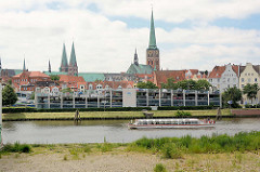Blick über die Kanaltrave von Lübeck - Parkhaus am Kanalufer, Kirchtürme der Stadt - ein Ausflugsschiff mit Touristen an Bord auf der Rundfahrt durch die Kanäle der Stadt.
