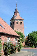 Kirchturm der St. Jacobikirche in Bleckede - im Vordergrund ein Fachwerkhaus mit blühenden Stockrosen.