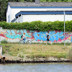 Mauer mit Graffiti am Kanalufer der Kanaltrave - Fahrradfahrer und Jogger.