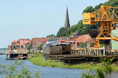 Werft an der Elbe / Lauenburg; ein Binnenschiff liegt zur Reparatur auf der Slipanlage / Helge, Werftkran - im Hintergrund Häuser und Kirchturm der Stadt.
