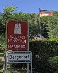 Hamburgs südöstliche Stadtgrenze; ein rotes Schild mit weisser Schrift "Freie und Hansestadt Hamburg" weist auf die Grenze zum Stadtstaat Hamburg hin. Die Burg mit den Türmen und Zinnen ist das Wappen Hamburgs. Das weisse Schild darunter zeigt de