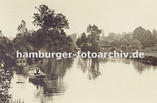 historisches Bild aus Hamburg Bergedorf ca. 1890; ein Mann mit Hut fährt im Ruderboot auf der Bille. Am Flussufer stehen zwischen den Bäumen Bauernhäuser und Fachwerkhäuser, im Hintergrund ist der Kirchturm der St. Petri und Pauli Kirche von Berg