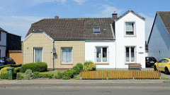 Doppelhaus mit unterschiedlicher Fassadengestaltung - gelber Klinker und weisse Putzfassade, Hecke oder Zaun; Architektur in Brunsbüttel, Kreis Dithmarschen.