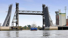 Ein Frachter fährt von der Rethe in den Reiherstieg in Hamburg Wilhelmsburg ein - die neue Brücke ist hochgeklappt, dahinter ist die alte Hubbrücke hochgefahren.
