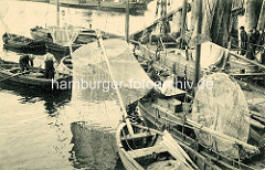 Hafenfischer bei ihren Booten im Hafen von Hamburg Altona - ein Fischer sitzt auf dem Bug eines Segelboots und repariert sein Wurfnetz.