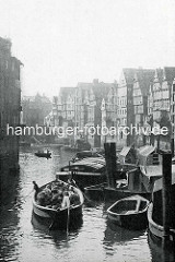 Altes Foto vom Nikolaifleet, re. die Kaufmannshäuser / Speicher an der Deichstraße; Schuten und Arbeitsboote im Fleet - ein Holzboot beladen mit Körben wird von den Schiffsführern durchs Wasser gestakt.