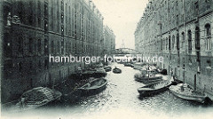 Historisches Foto vom Kehrwiederfleet mit Blick Richtung Elbe;  Schuten beladen mit Säcken liegen an den Speichern; Säcke werden mit Winden in das Lager hinaufgezogen.