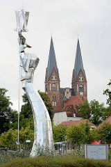 Moderne Edelstahlskulptur Parzival am See - Höhe 17 Meter, Künstler Matthias Zágon Hohl-Stein. Einweihung 1998 zur Verleihung des Namens Fontanestadt. Im Hintergrund die Klosterkirche Sankt Trinitatis.