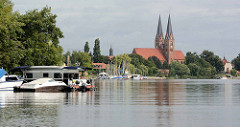Ufer mit Bootssteg und Segelbooten am Ruppiner See. Kirchtürme der Klosterkirche St. Trinitatis von Neuruppin.