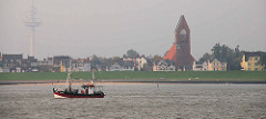 Fischkutter in Fahrt vor Cuxhaven. Im Hintergrund die Strandpromenade mit Garnisonskirche St. Petri.