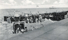 Historische Ansicht vom Strandleben in Duhnen - große Sandburg mit Muschelaufschrift Burg Kränzchen unter uns; Gruppe mit Frauen in Bademänteln - verschiedene Flaggen.