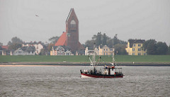 Fischkutter in Fahrt vor Cuxhaven. Im Hintergrund die Strandpromenade mit Garnisonskirche St. Petri.