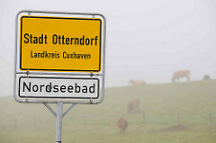 Stadtgrenze / Ortsschild Stadt Otterndorf, Landkreis Cuxhaven - Nordseebad; im Hintergrund Kühe auf dem Deich im Nebel.