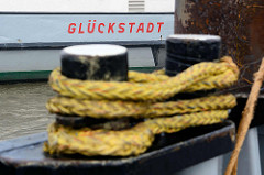 Poller mit Tau - Klampe belegt am Fähranleger, Schriftzug Glückstadt.