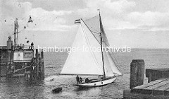 Ein Sportboot Segelschiff mit Ruderboot im Schlepp läuft aus dem Hafen von Cuxhaven aus - es passiert die Hafenmole der Alte Liebe.